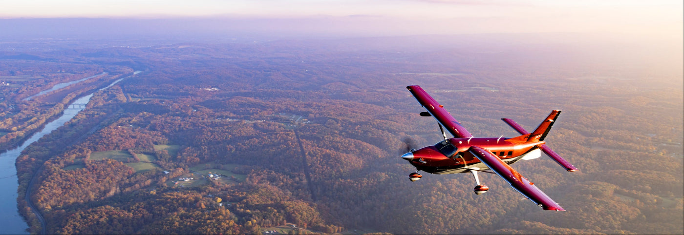 Small airplane flying over a landscape with a river and trees